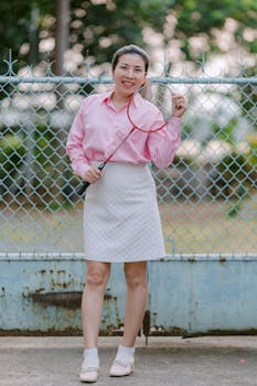 Smiling woman holding a badminton racket against a chain-link fence.