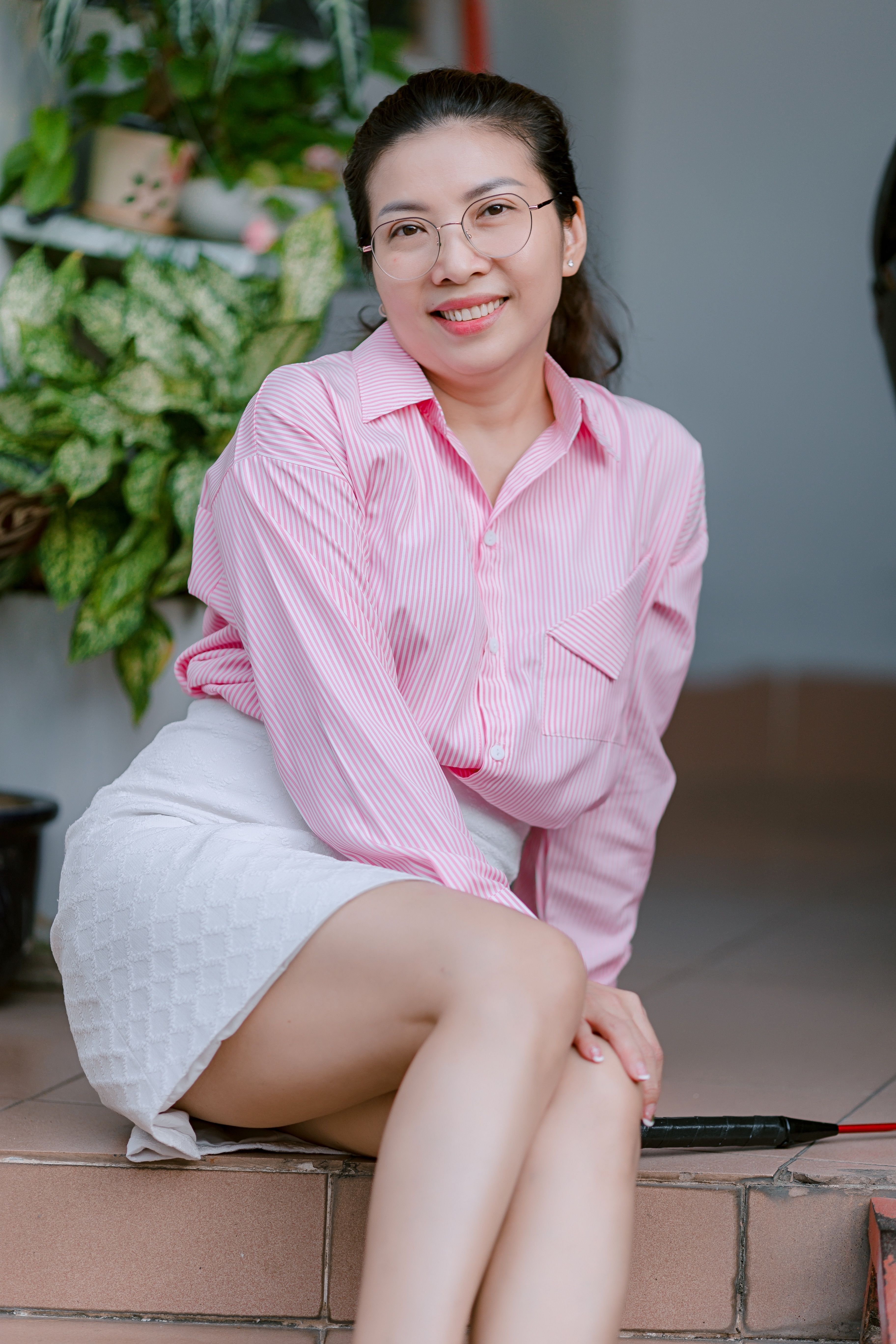 A woman in a pink shirt and white skirt sitting with a friendly smile indoors.