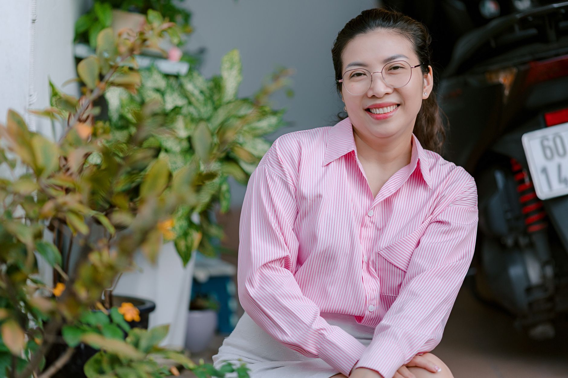 Cheerful woman with glasses posing indoors near foliage.