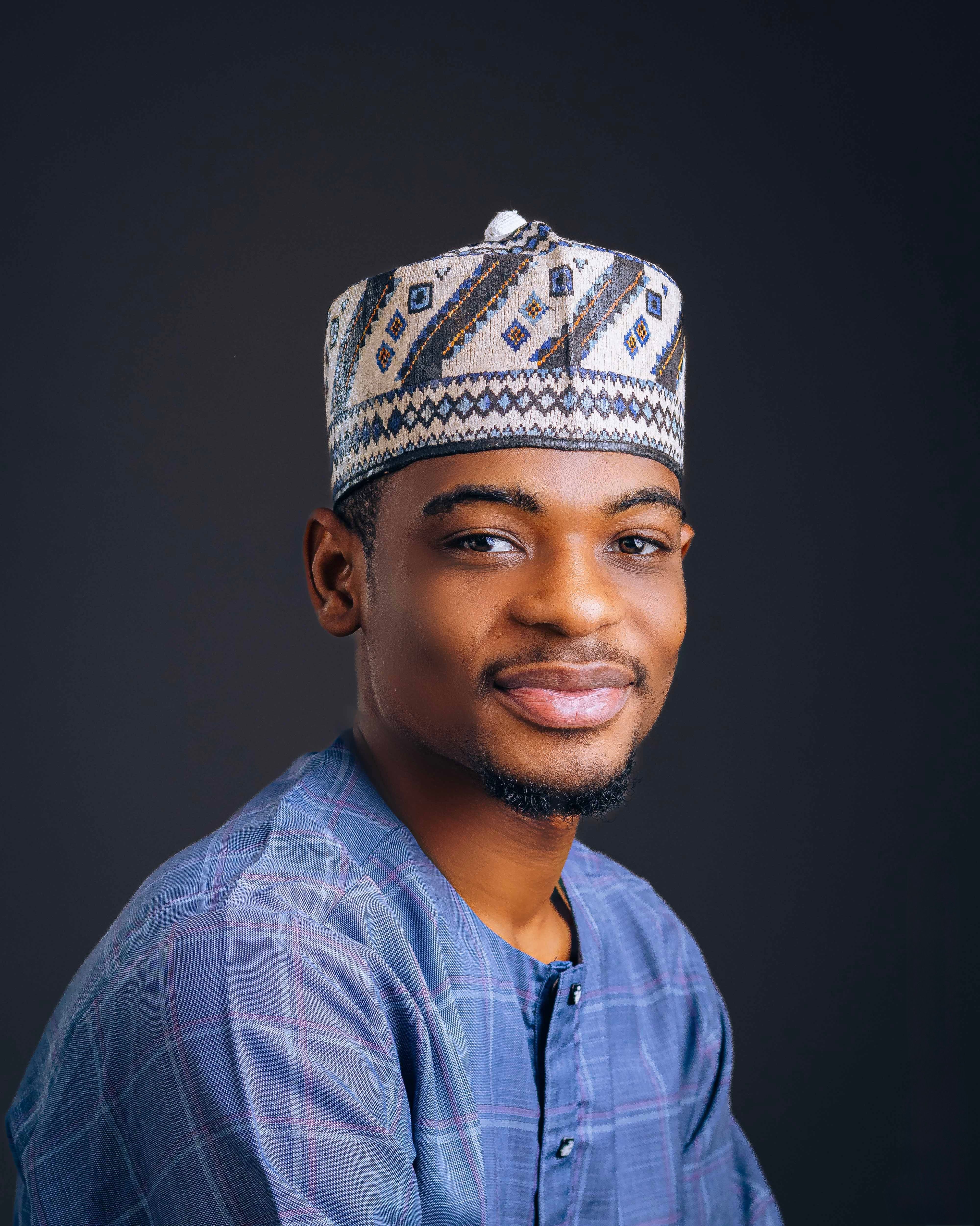 Portrait of a smiling man wearing traditional African attire on a dark background.
