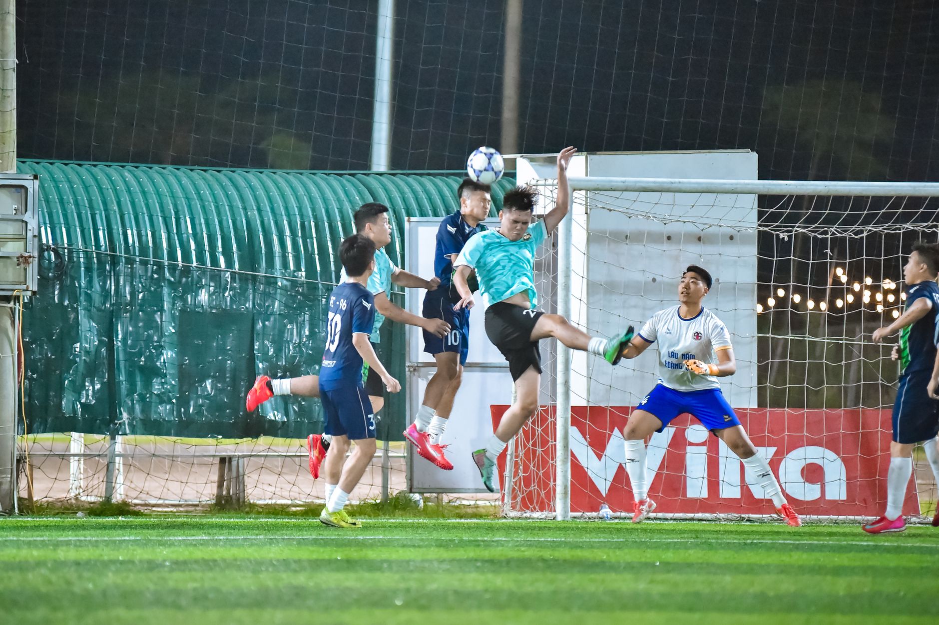 Players in an intense football game going for a header, captured in Hà Nội at night.