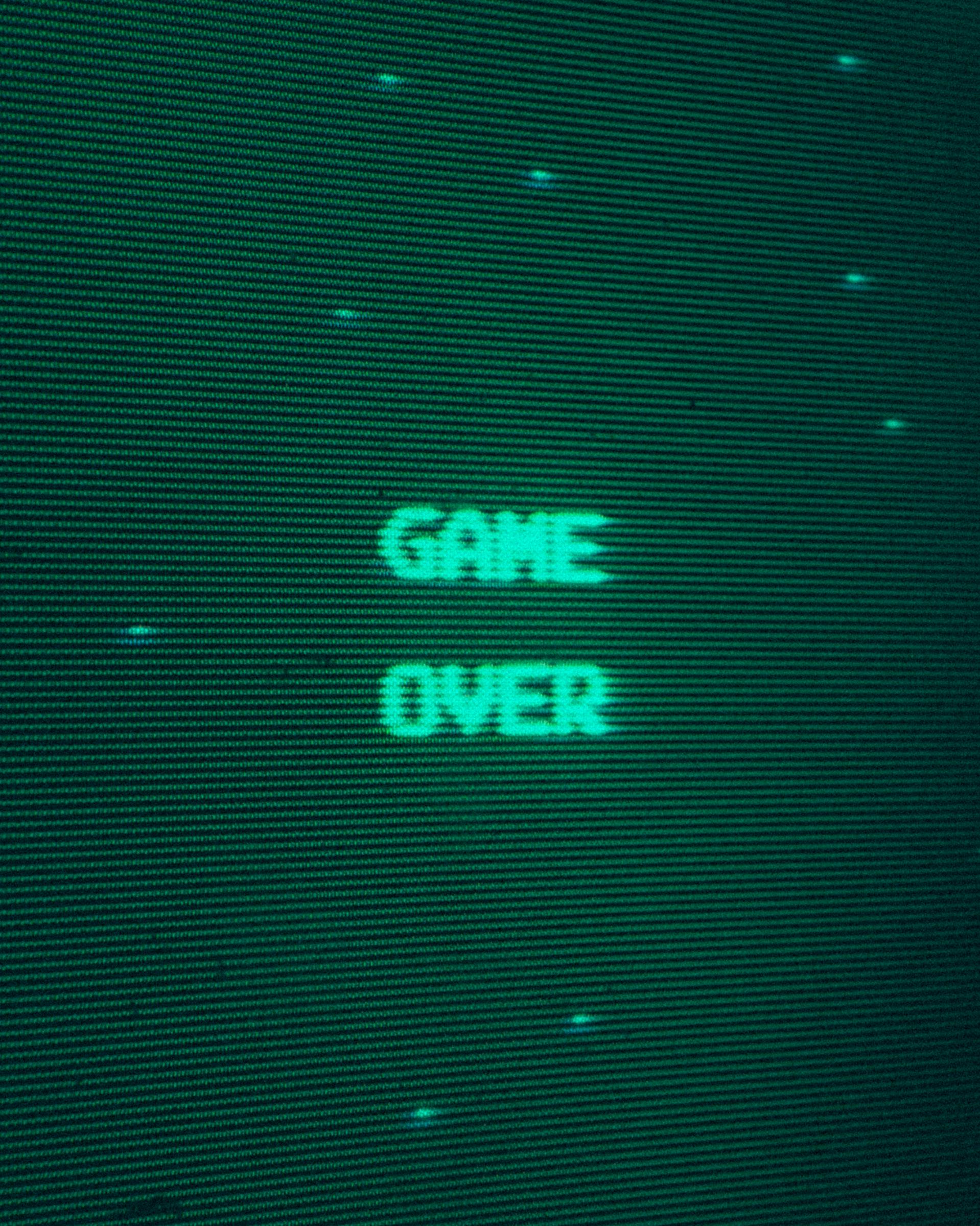 Gratis Primo piano della schermata "Game Over" di un videogioco arcade retrò in verde, che evoca la nostalgia dei videogiochi classici. Foto a disposizione