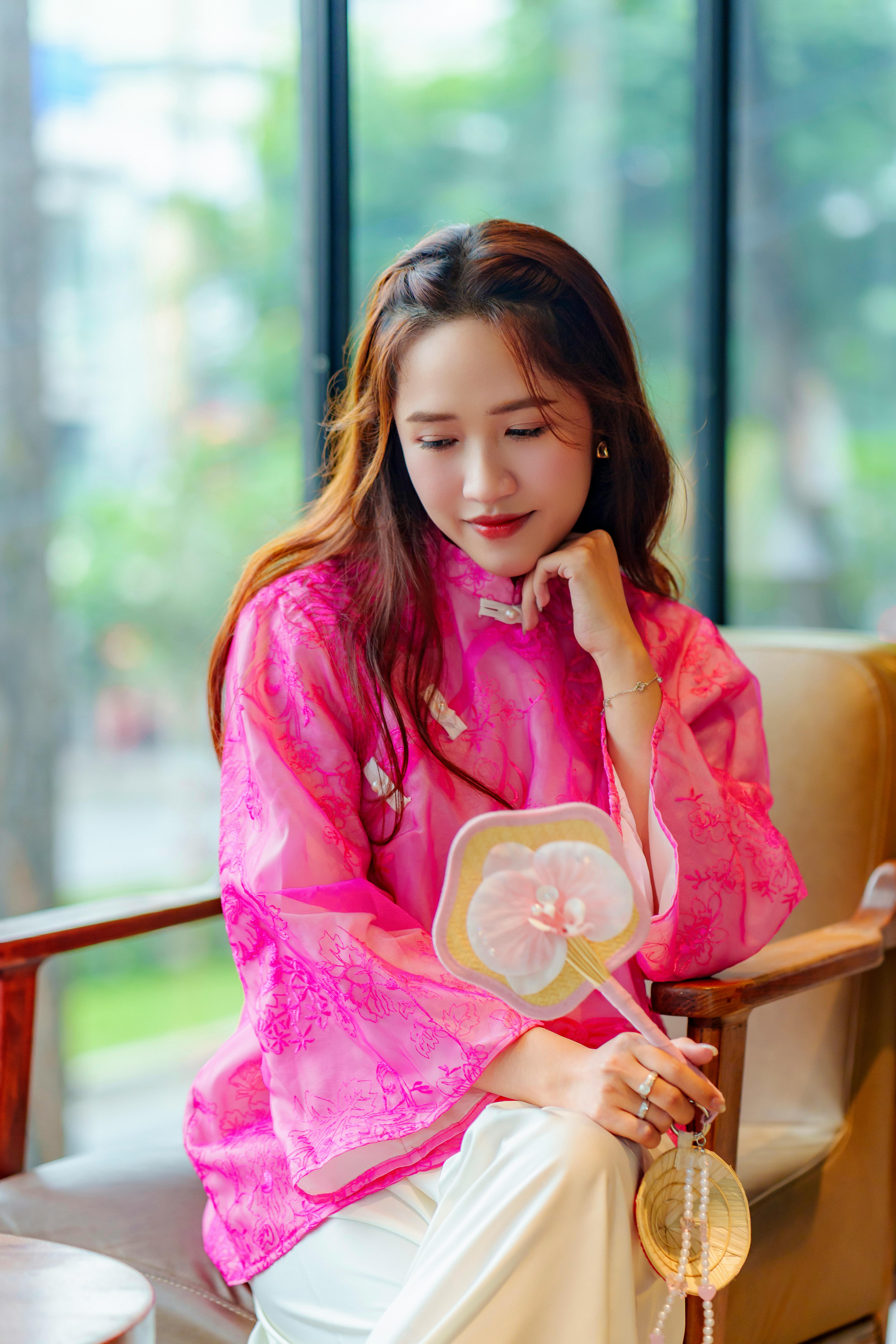 Portrait of a young woman wearing a vibrant pink áo dài indoors, reflecting cultural elegance.