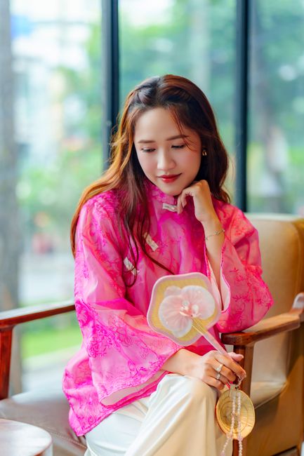 Portrait of a young woman wearing a vibrant pink áo dài indoors, reflecting cultural elegance.