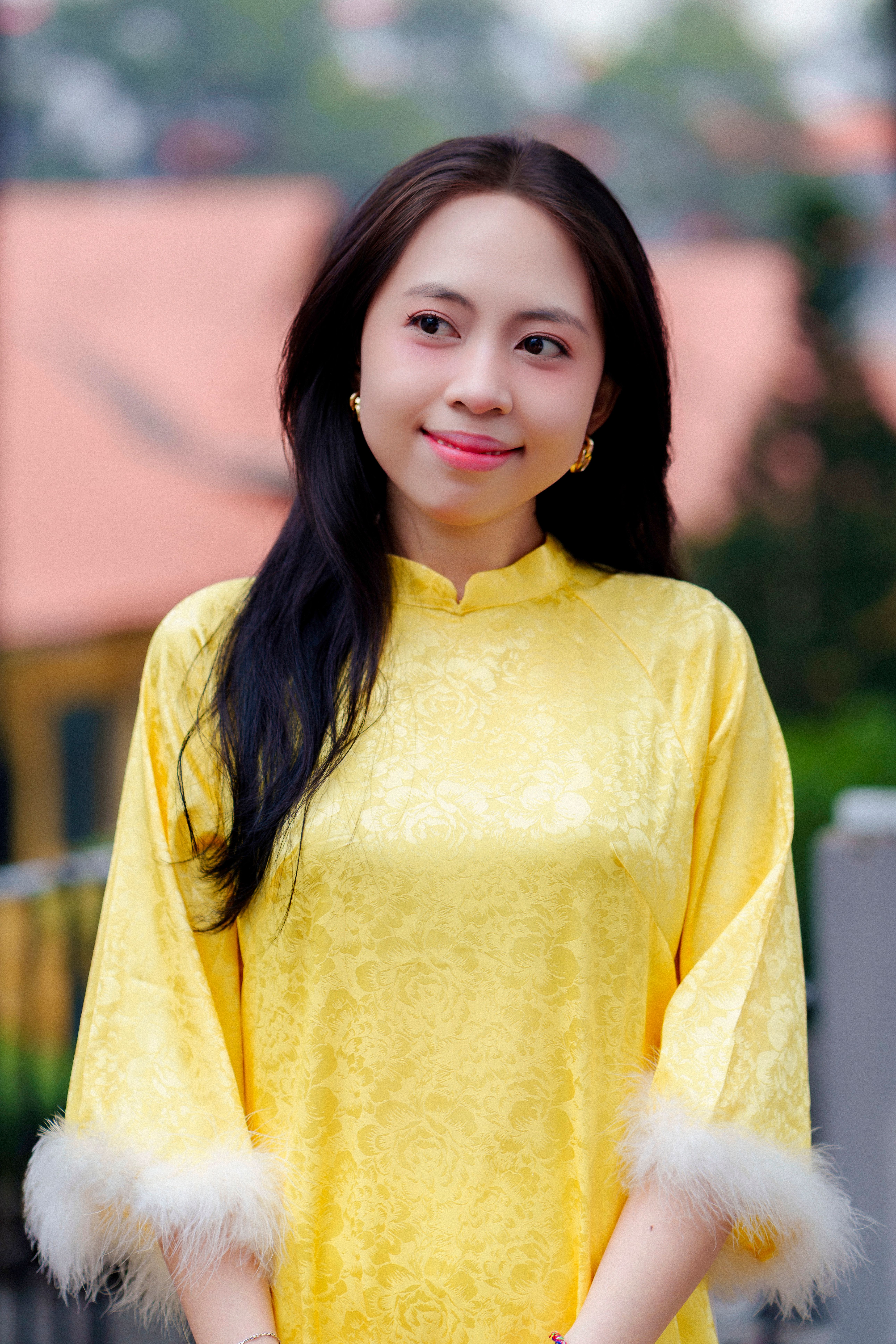 A woman in a yellow áo dài smiles outdoors in Ho Chi Minh City.