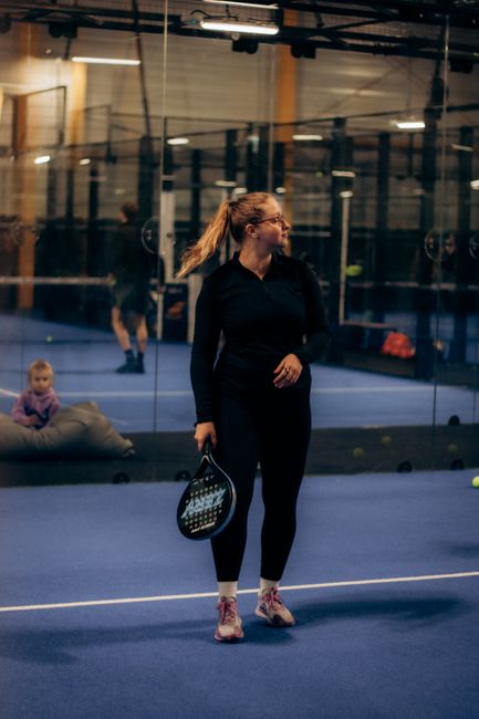 Woman holding a padel racket on an indoor court, focused on the game.