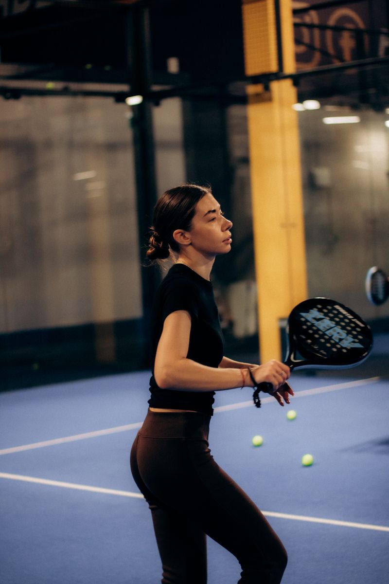 Focused woman playing paddle tennis on an indoor court, holding racket in active pose.