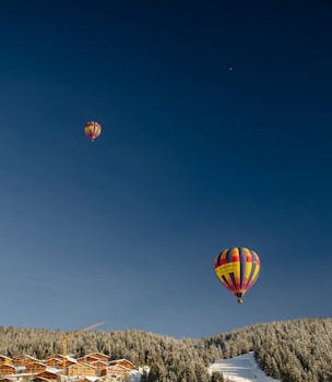 Colorful hot air balloons soaring above a snowy forest and chalet rooftops.
