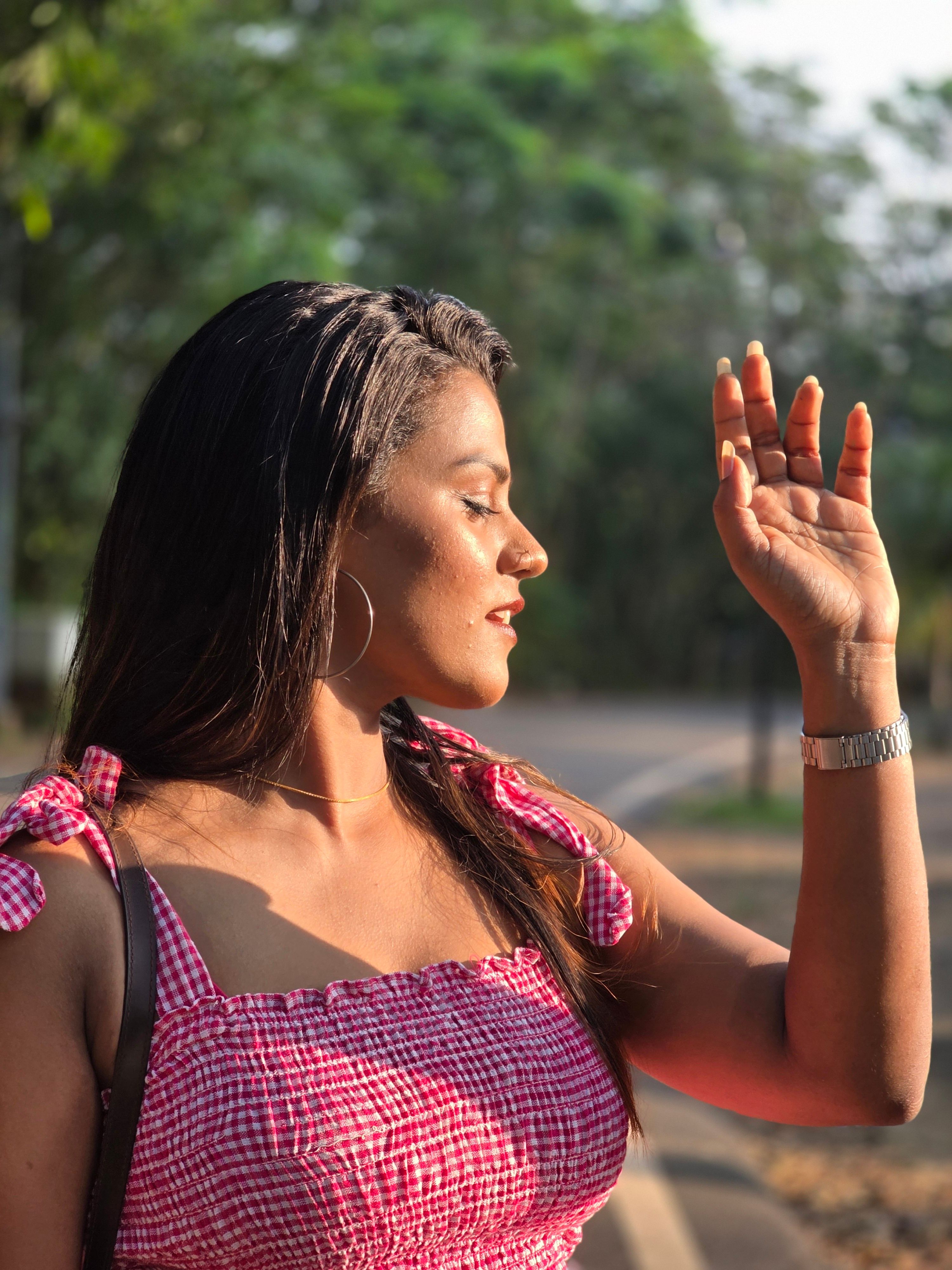 Woman in red dress enjoying the sunlight with a serene expression outdoors in a summer setting.