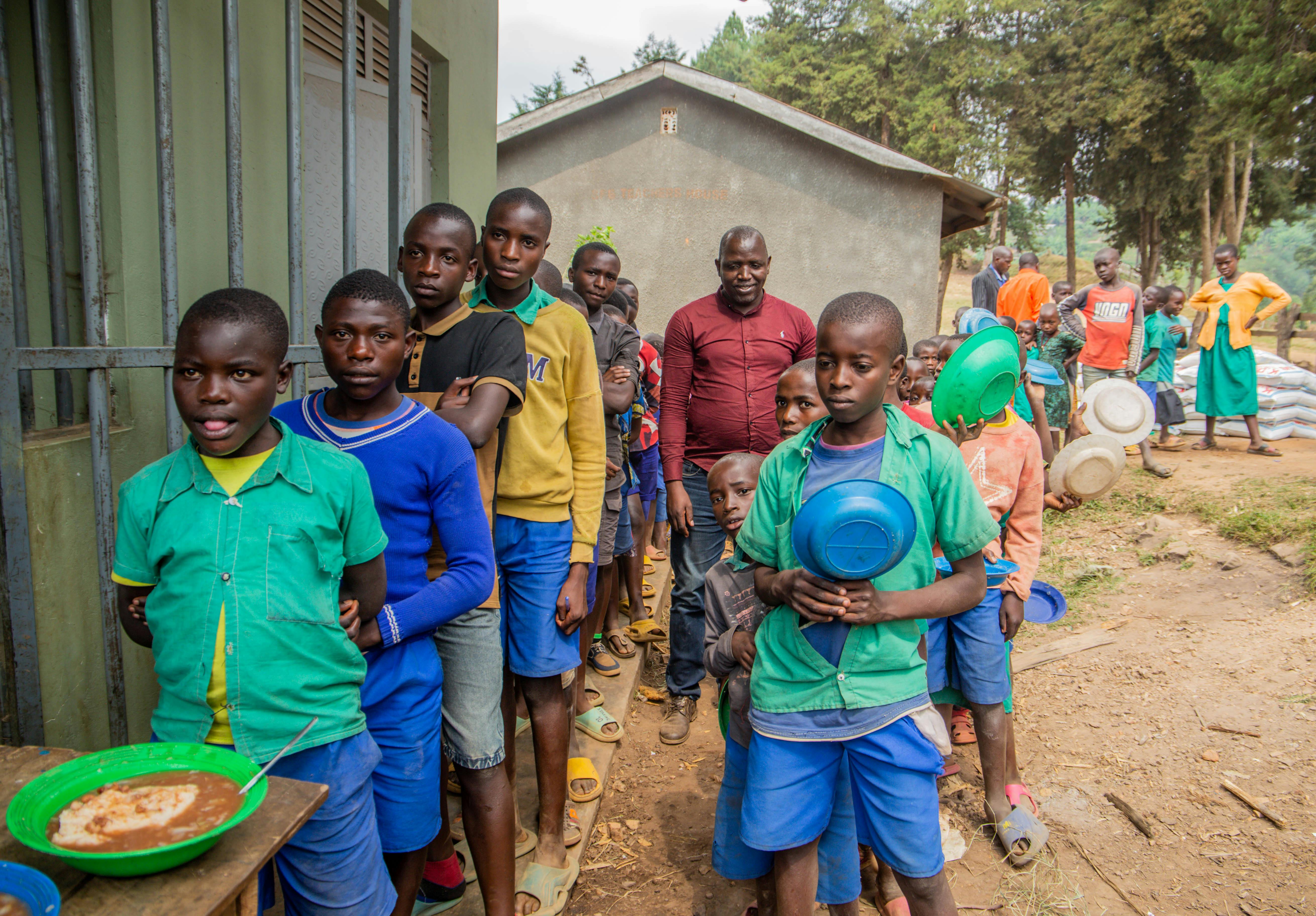 Children and adults waiting in line for food distribution outdoors, reflecting community support.