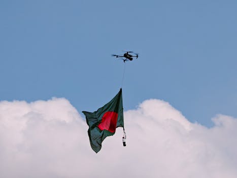 A drone flying the Bangladesh flag high against a backdrop of clear blue sky and fluffy clouds.