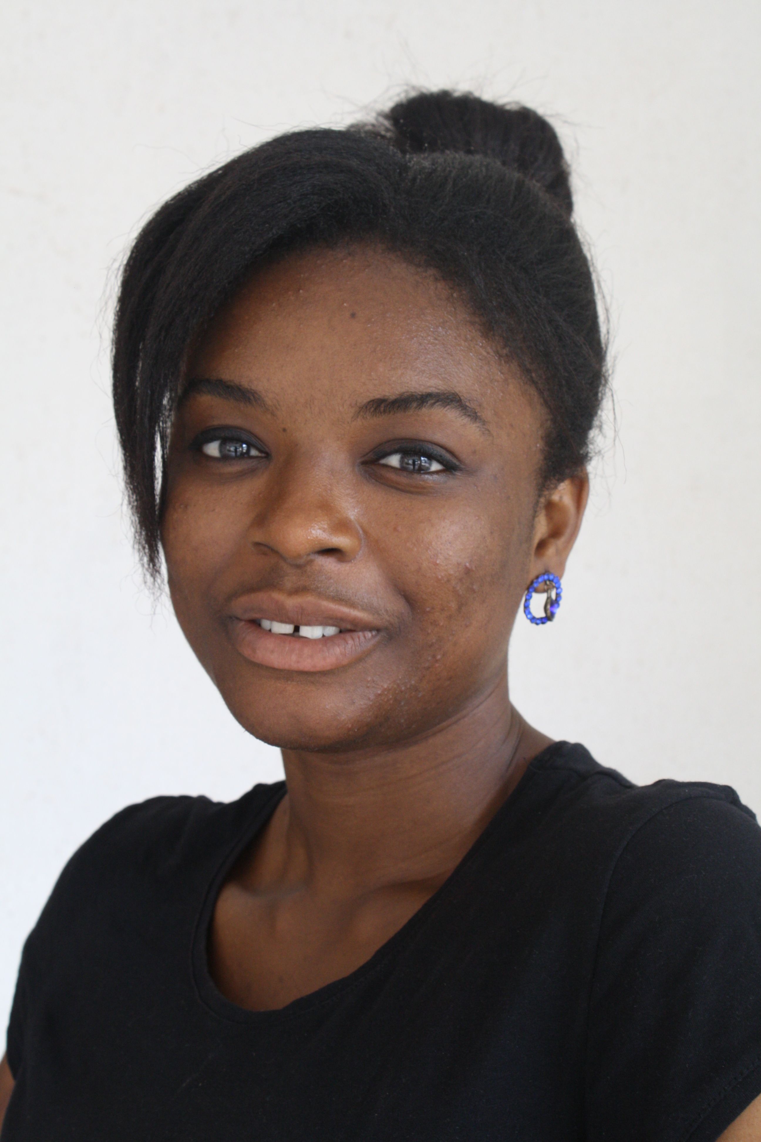 Portrait of a smiling woman with a natural hairstyle and blue earrings against a plain background.