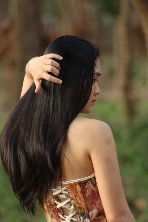 Free A woman with long, flowing hair poses gracefully outdoors, wearing a floral dress. Stock Photo
