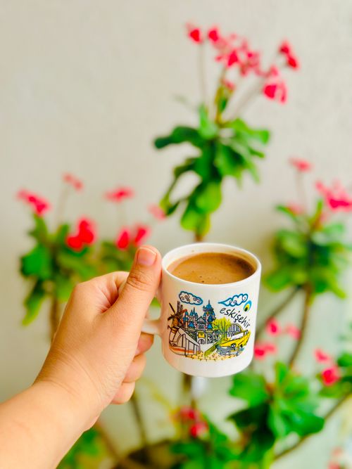 Free Hand holds a decorative cup of coffee against a vibrant floral backdrop. Stock Photo