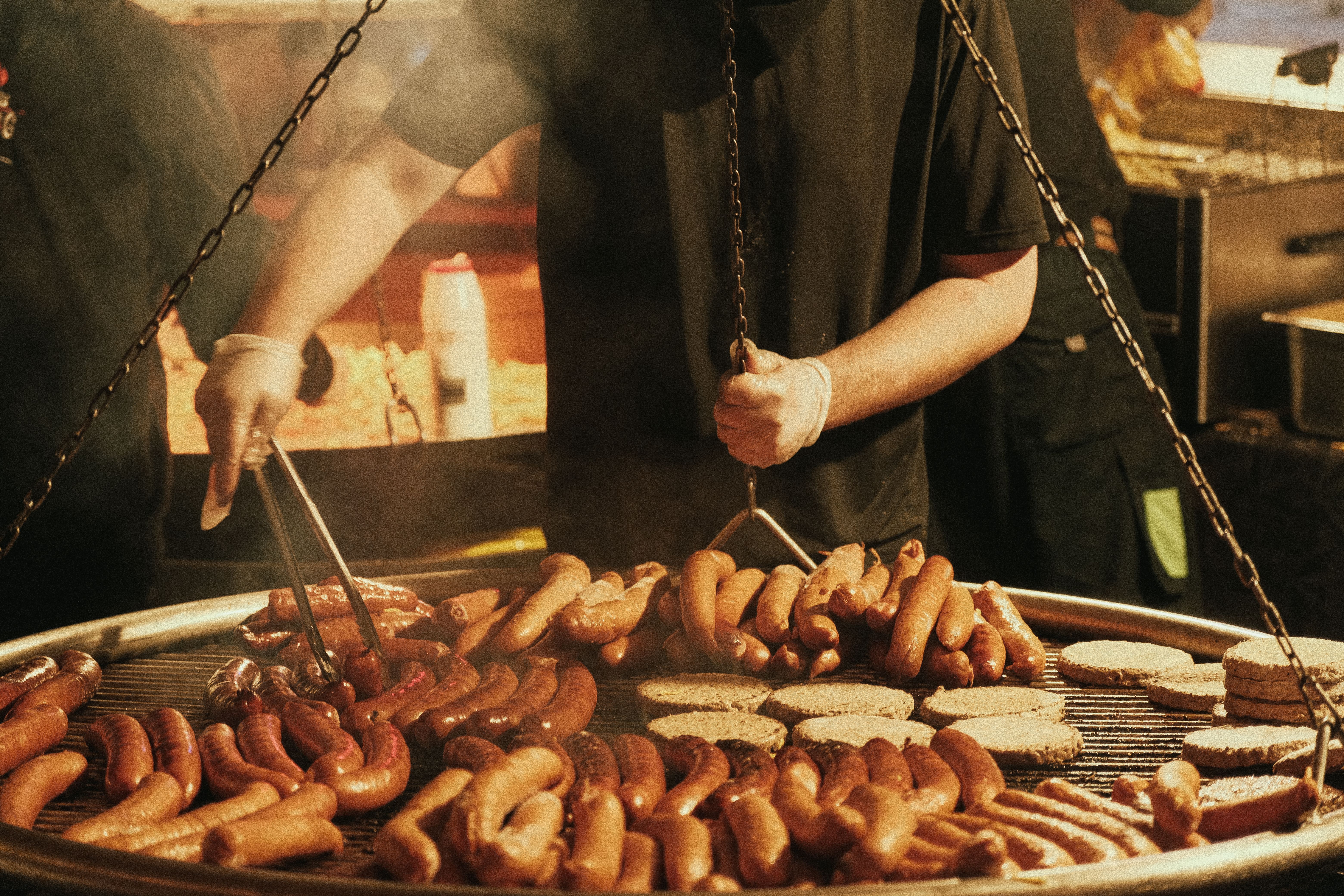 A street vendor grills an assortment of sausages at a vibrant Christmas night market, filling the air with enticing aromas.