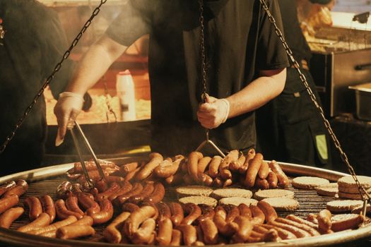 A street vendor grills an assortment of sausages at a vibrant Christmas night market, filling the air with enticing aromas.