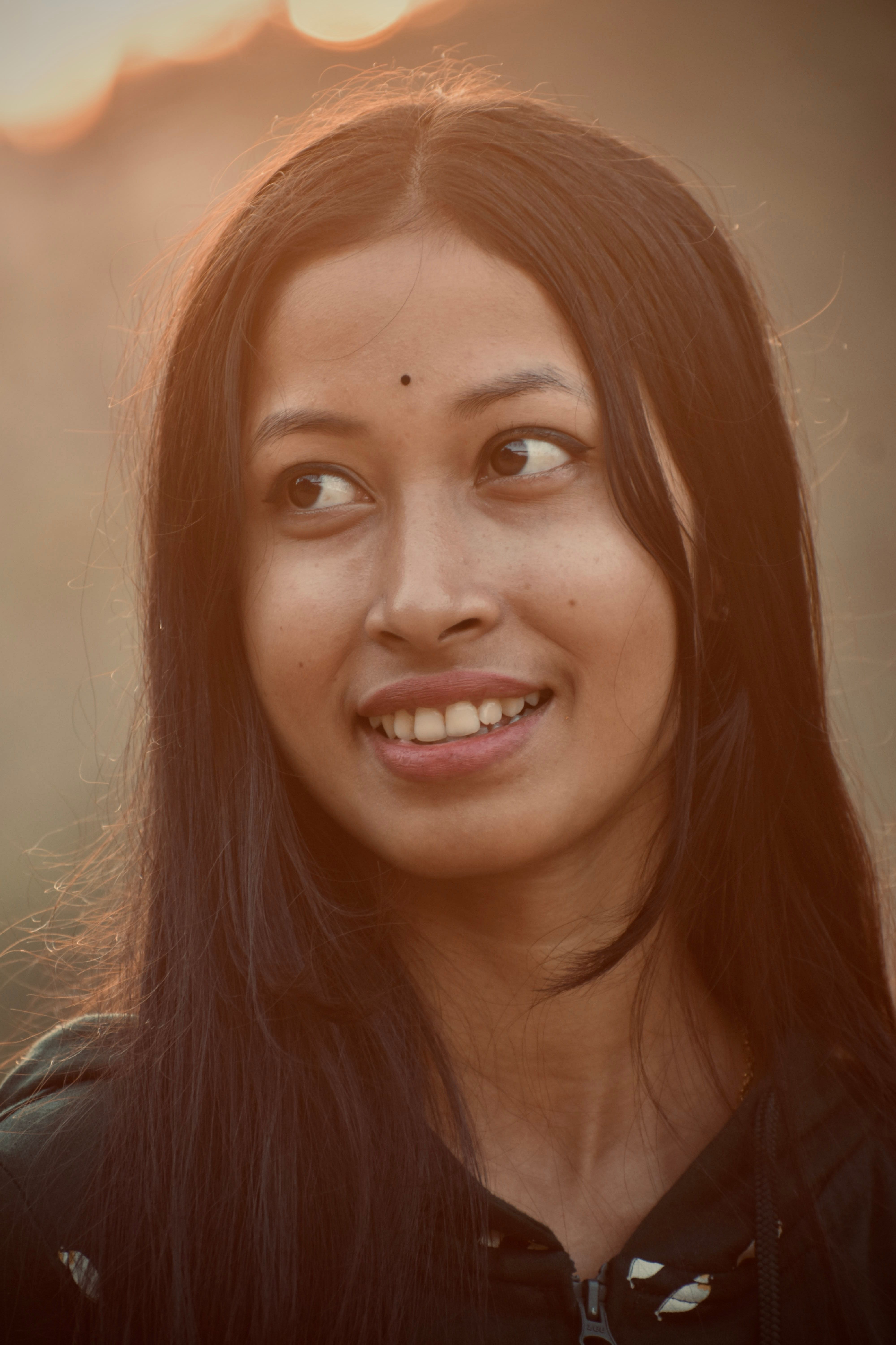 Close-up portrait of a woman smiling warmly against a soft sunset background.