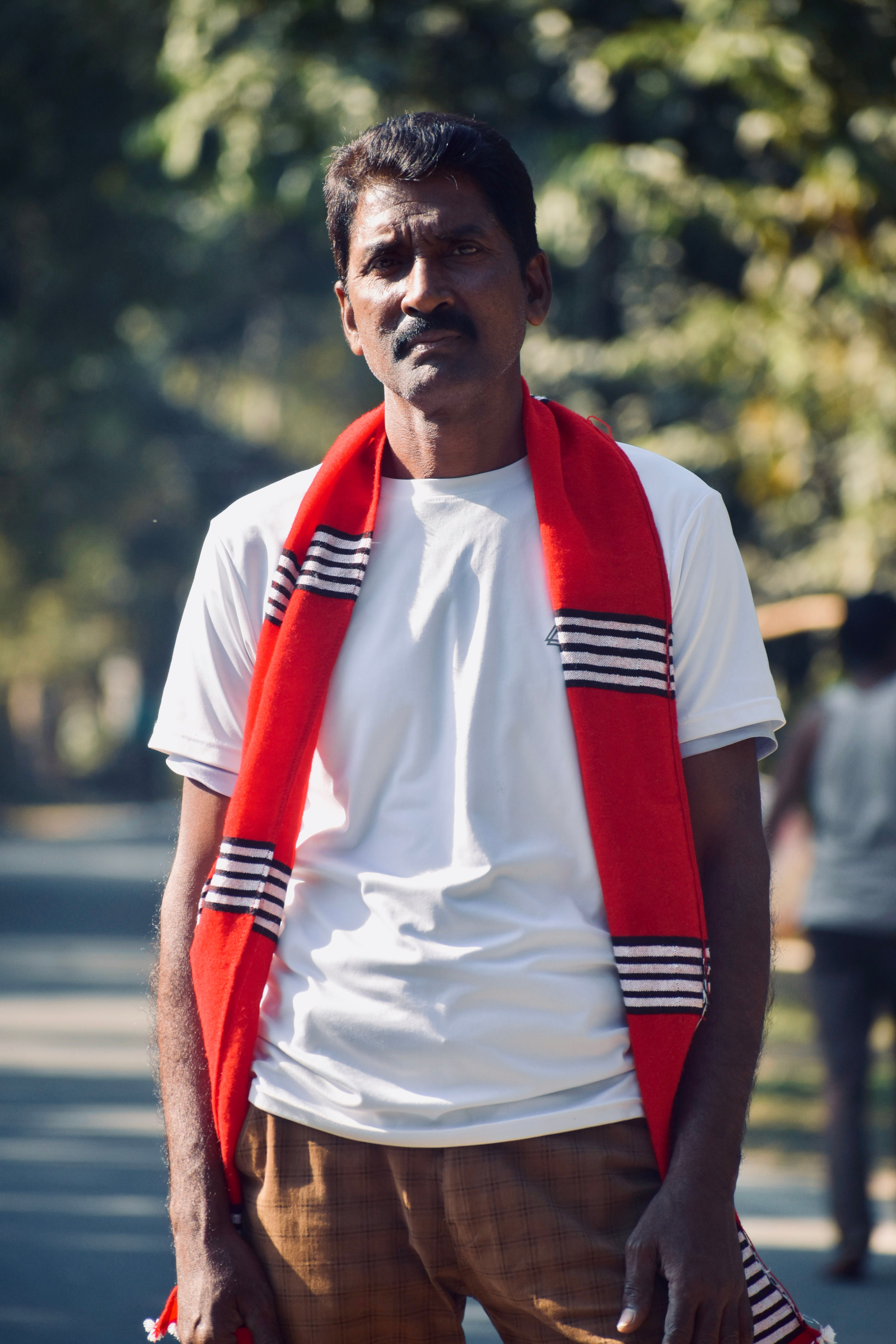 South Asian man standing outdoors in Assam, India, wearing a red scarf and white shirt.