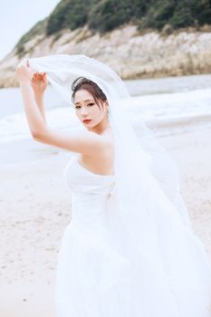 美丽的新娘穿着白色婚纱，在风景如画的沙滩上举着面纱。 - 相关推荐