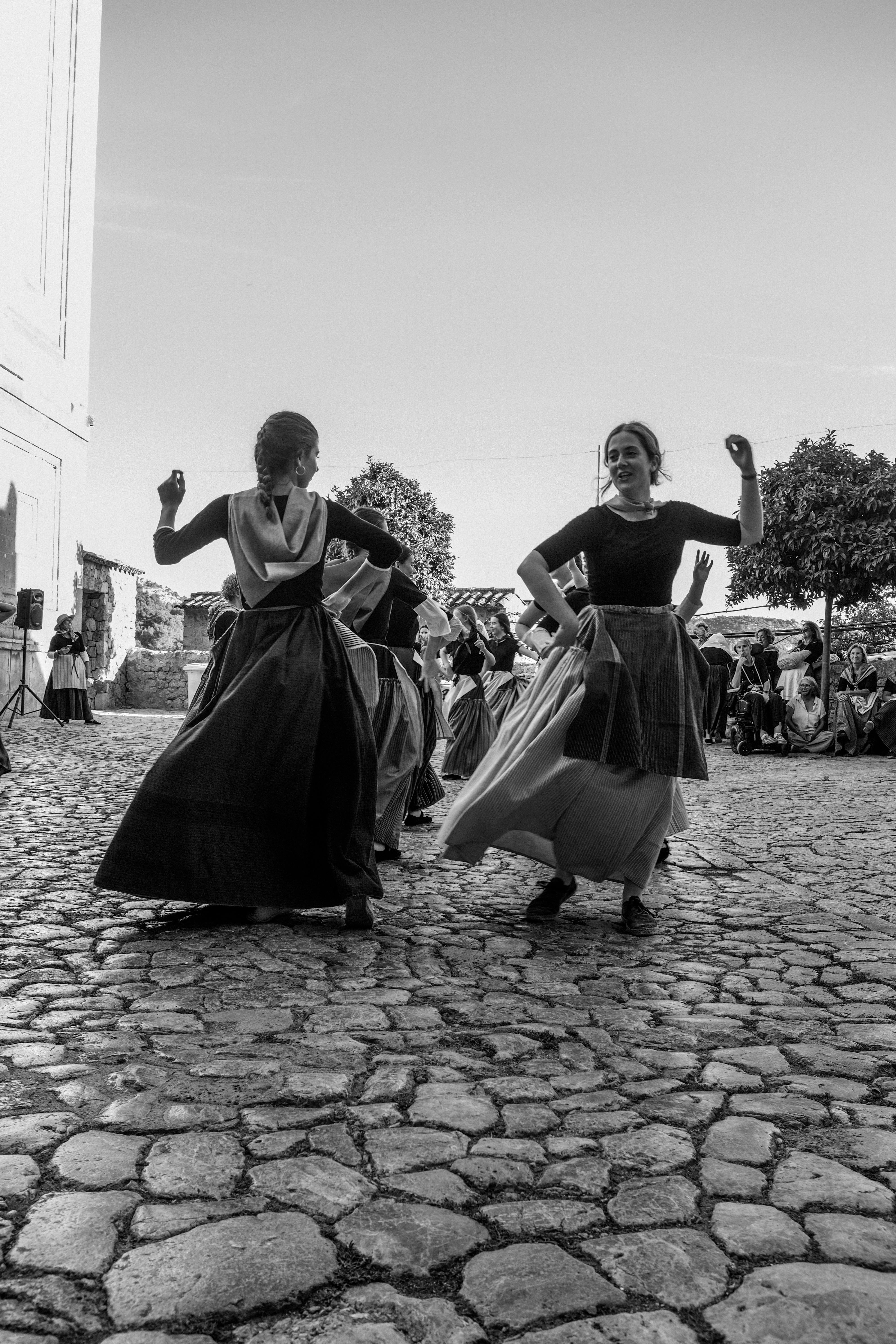 Black and white photo capturing traditional folk dancers on cobblestone street.