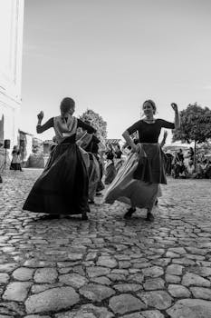 Black and white photo capturing traditional folk dancers on cobblestone street.