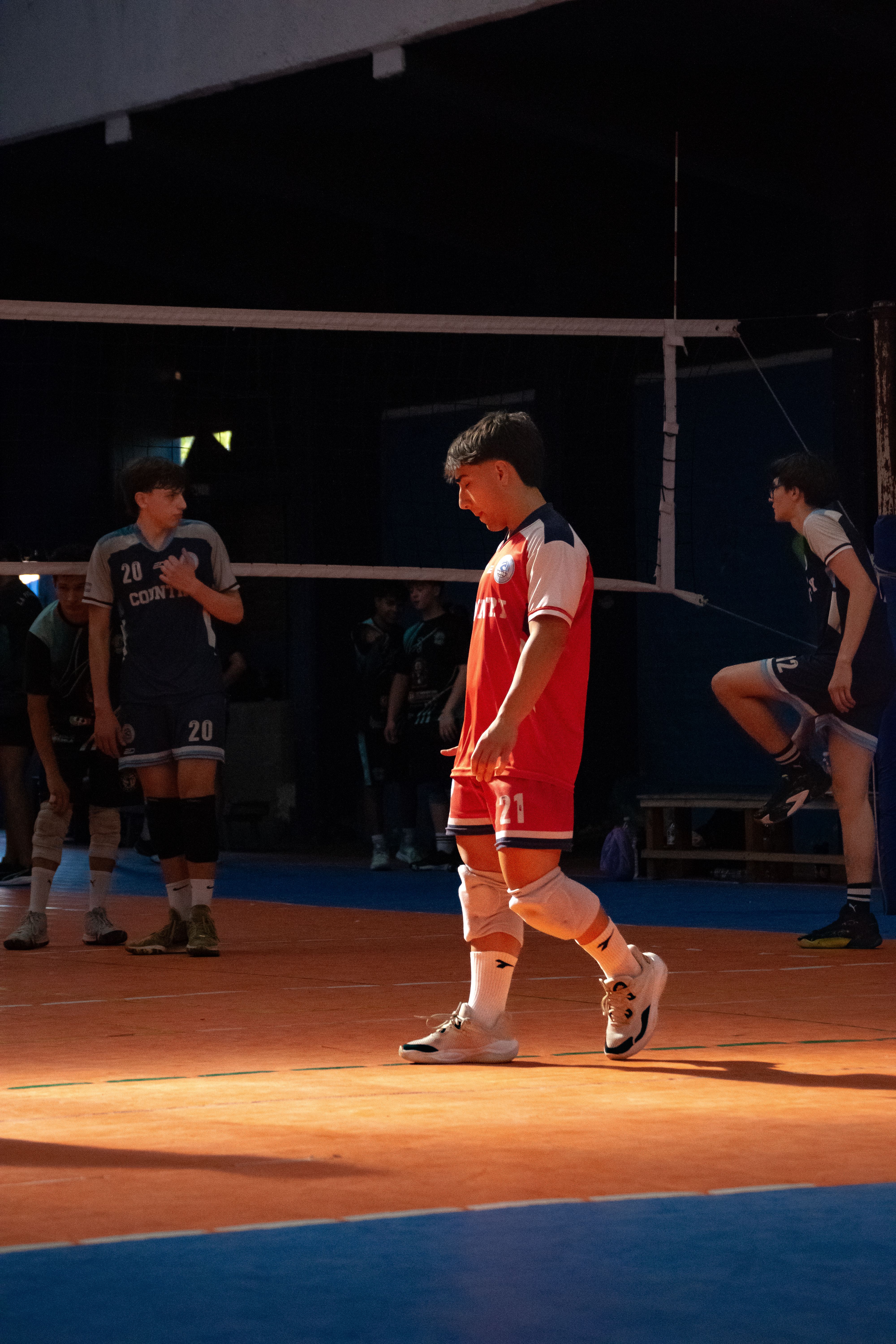 Players in an indoor volleyball match illuminated by dramatic lighting.