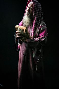Elderly man with a beard and headscarf holding a religious book, in contemplation.