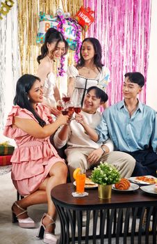 A lively indoor birthday celebration with friends toasting with drinks, surrounded by festive decorations.