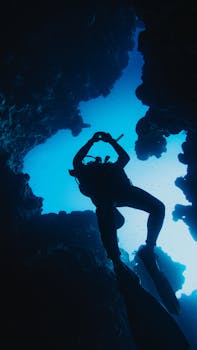 Scuba diver silhouetted against blue water while exploring an underwater cave.