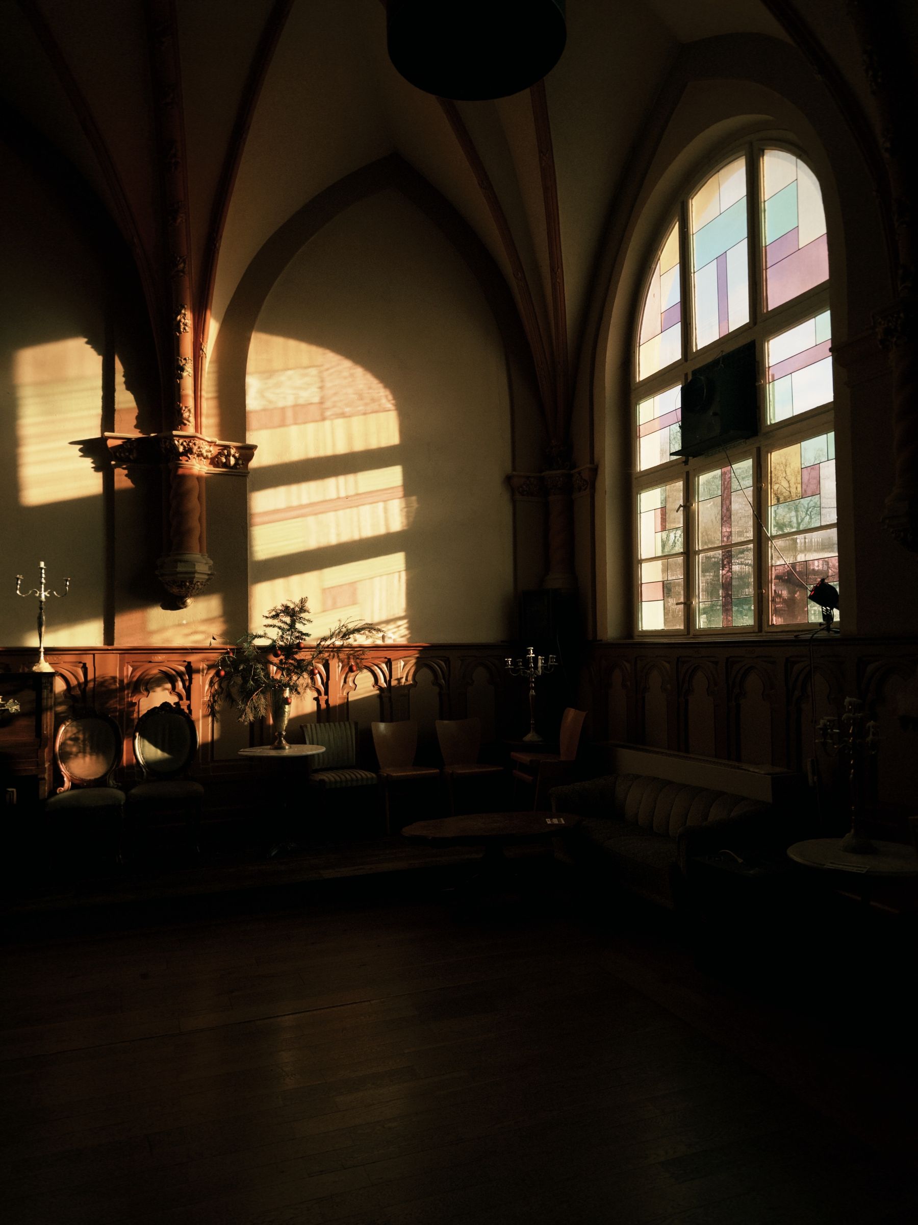 Historic room with pointed Gothic arches, stained glass, wood floor and warm sunlight