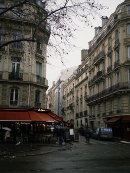 Explore a Parisian street with classic architecture and a cozy café on a moody day.