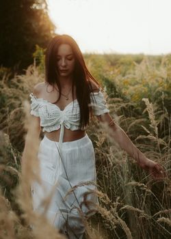 A serene portrait of a woman in a white dress walking through a field at sunset.
