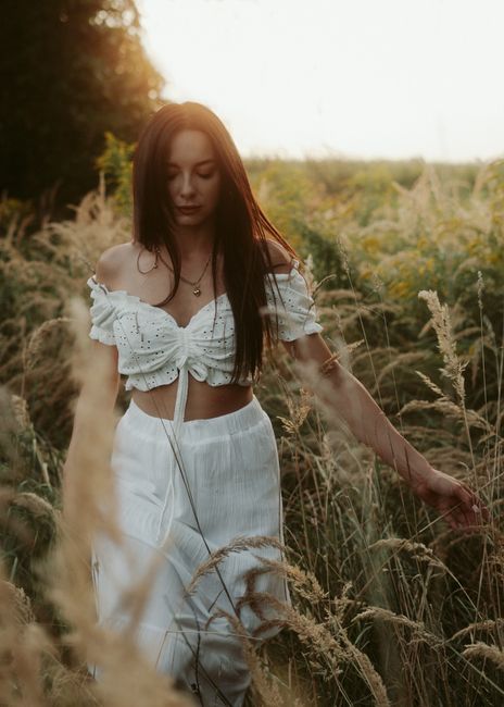 A serene portrait of a woman in a white dress walking through a field at sunset.