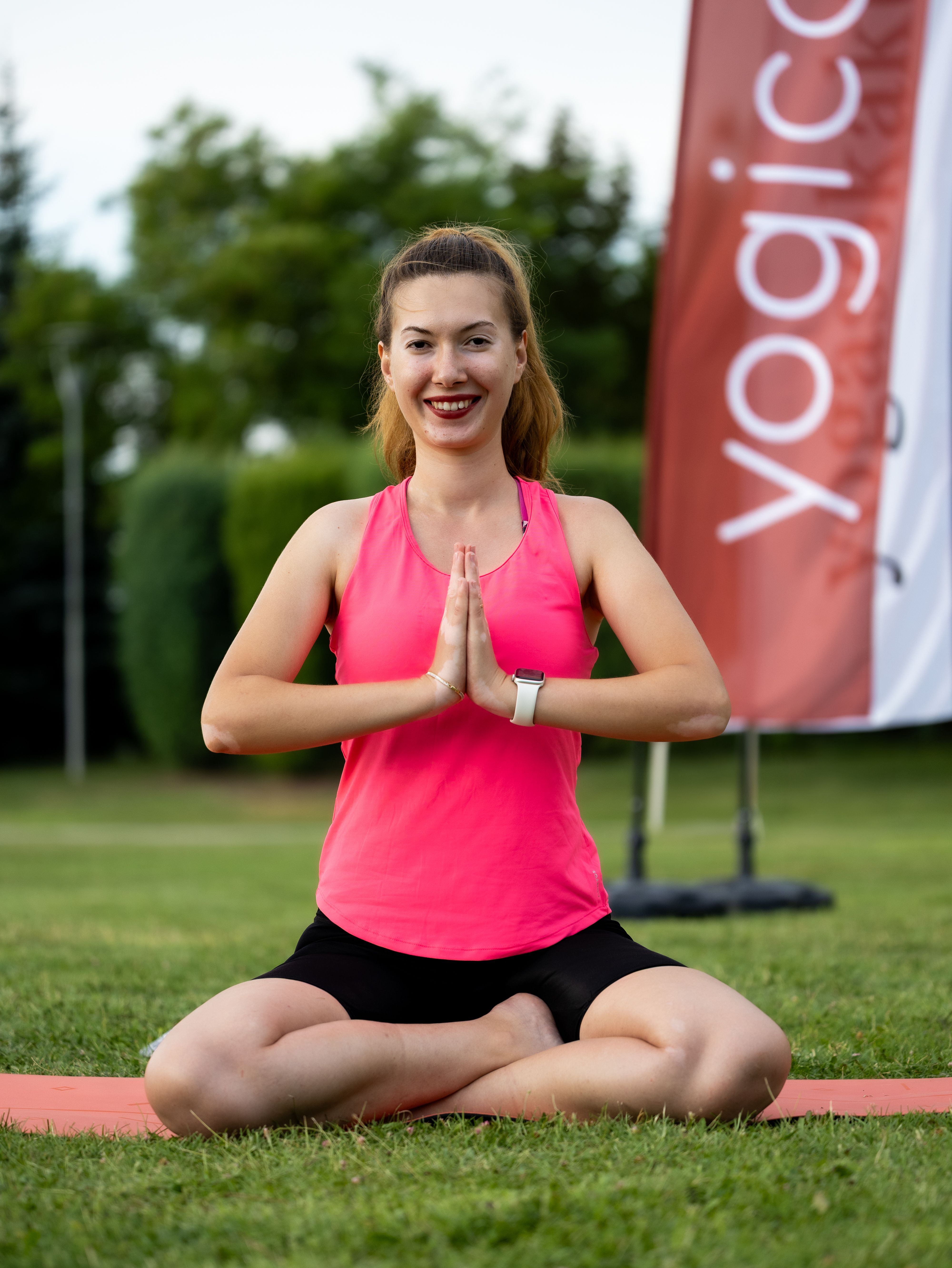 Smiling woman performing yoga on grass with hands in prayer position, embodying peaceful mindfulness outdoors.