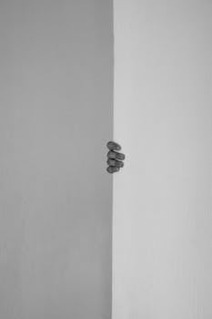 A hand grasping the edge of a white wall, creating an intriguing and minimalist composition.