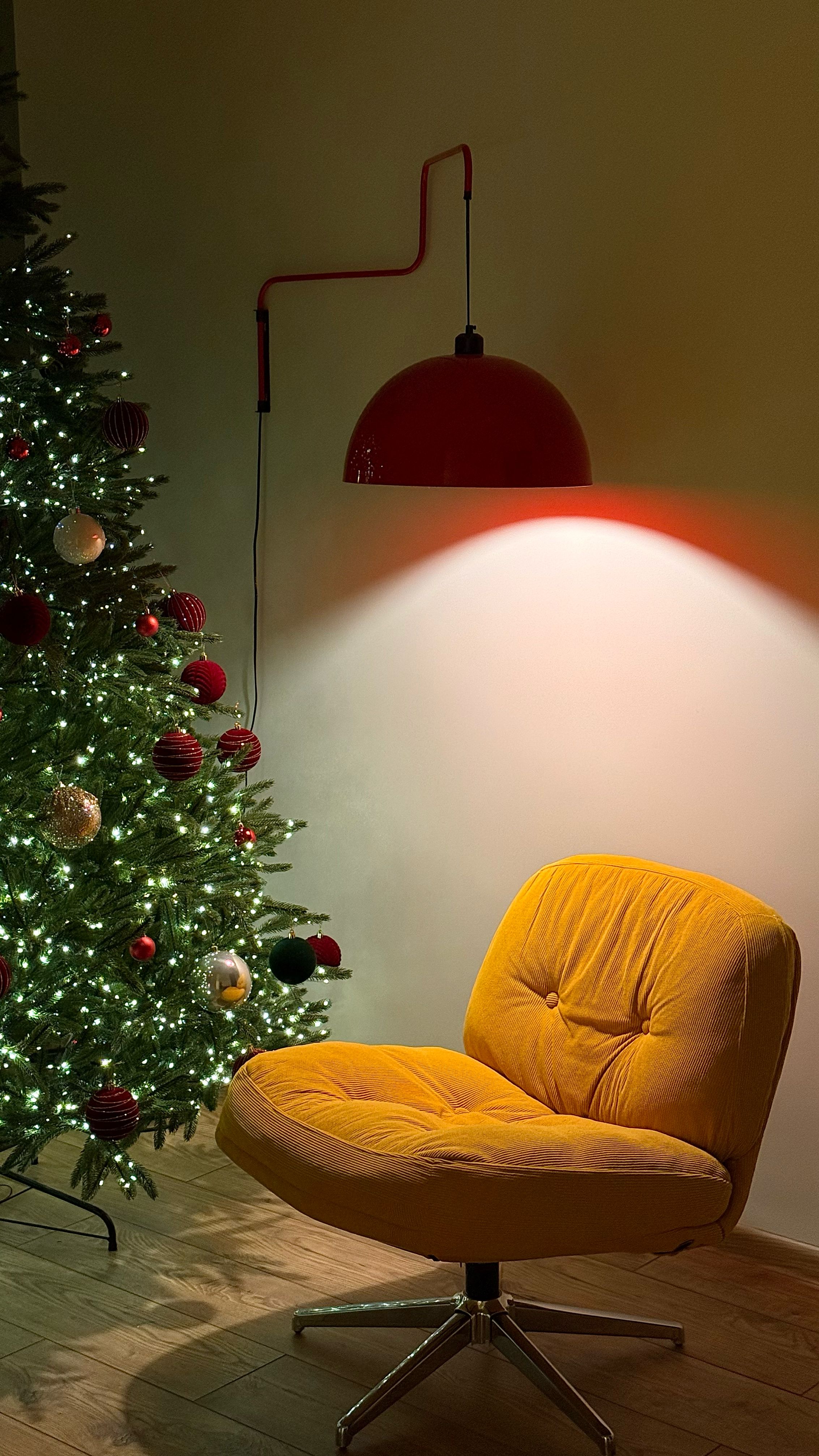 A festive Christmas scene with a decorated tree, cozy chair, and modern lamp casting warm light.