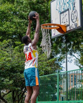 Basketball player dunking on an outdoor hoop during daytime.