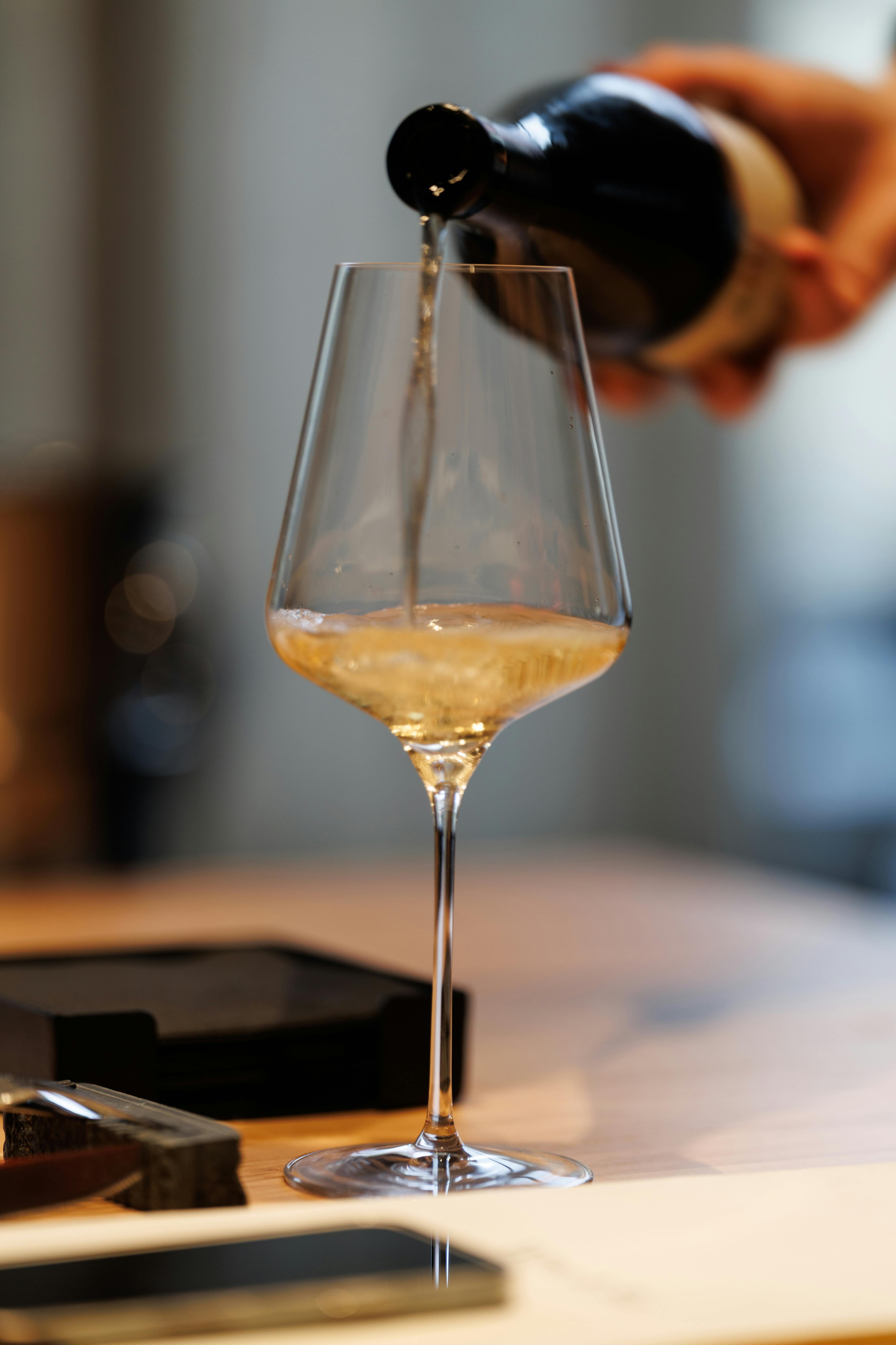 Close-up of a hand pouring white wine into a crystal glass on a table.