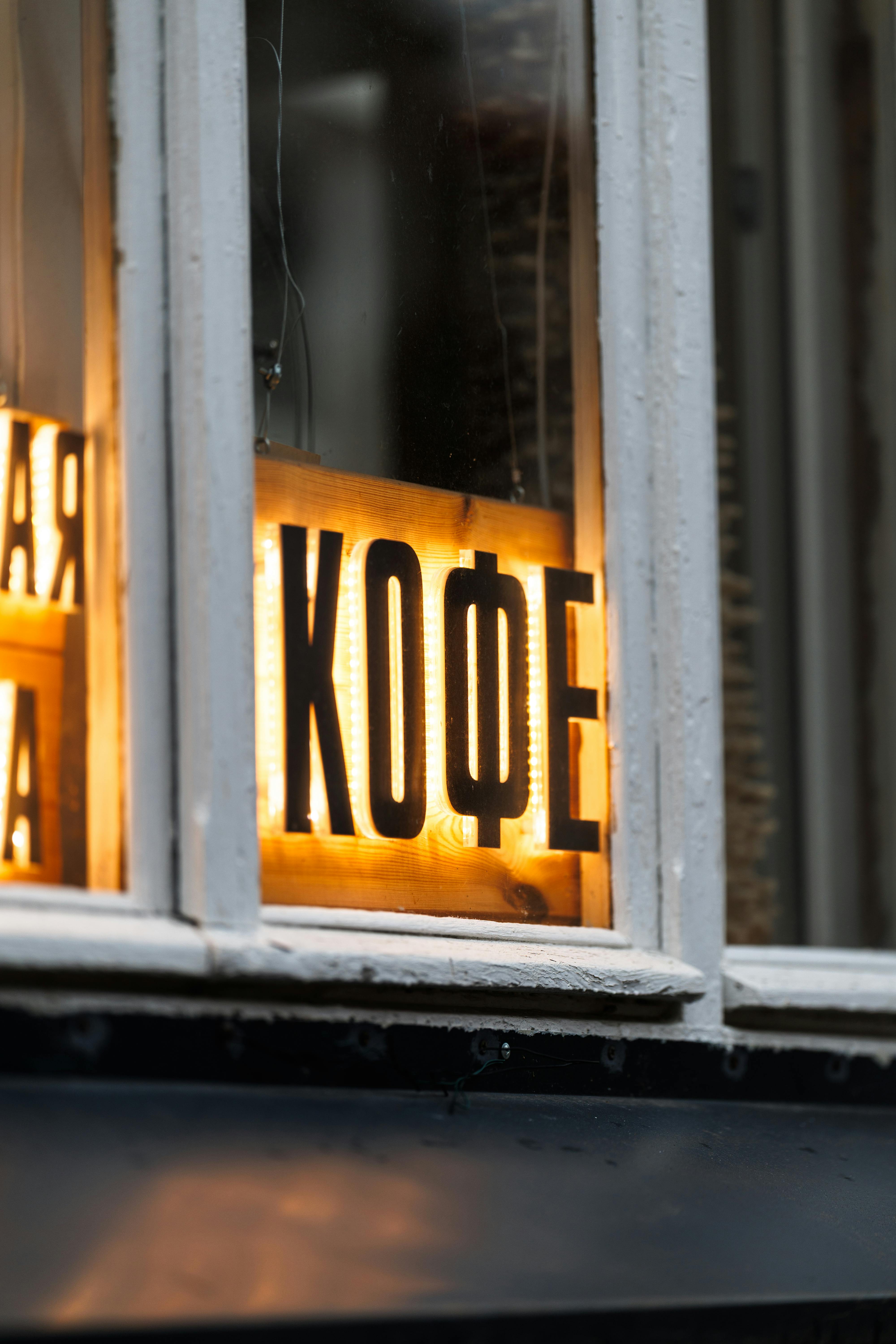 Illuminated sign in Cyrillic reading 'Кофе' in cozy cafe window, emitting warm light and ambiance.