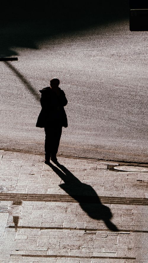 Free A dramatic silhouette of a person casting a long shadow on an urban street in daylight. Stock Photo