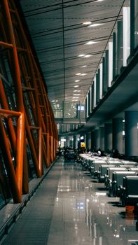 Empty airport terminal with orange beams, sleek design, and reflective floor surface.