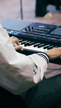 A musician wearing a white shirt plays an electronic keyboard indoors during the day.