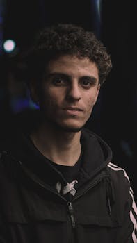 A detailed portrait of a young man with curly hair in a dimly lit setting, capturing a moody atmosphere.