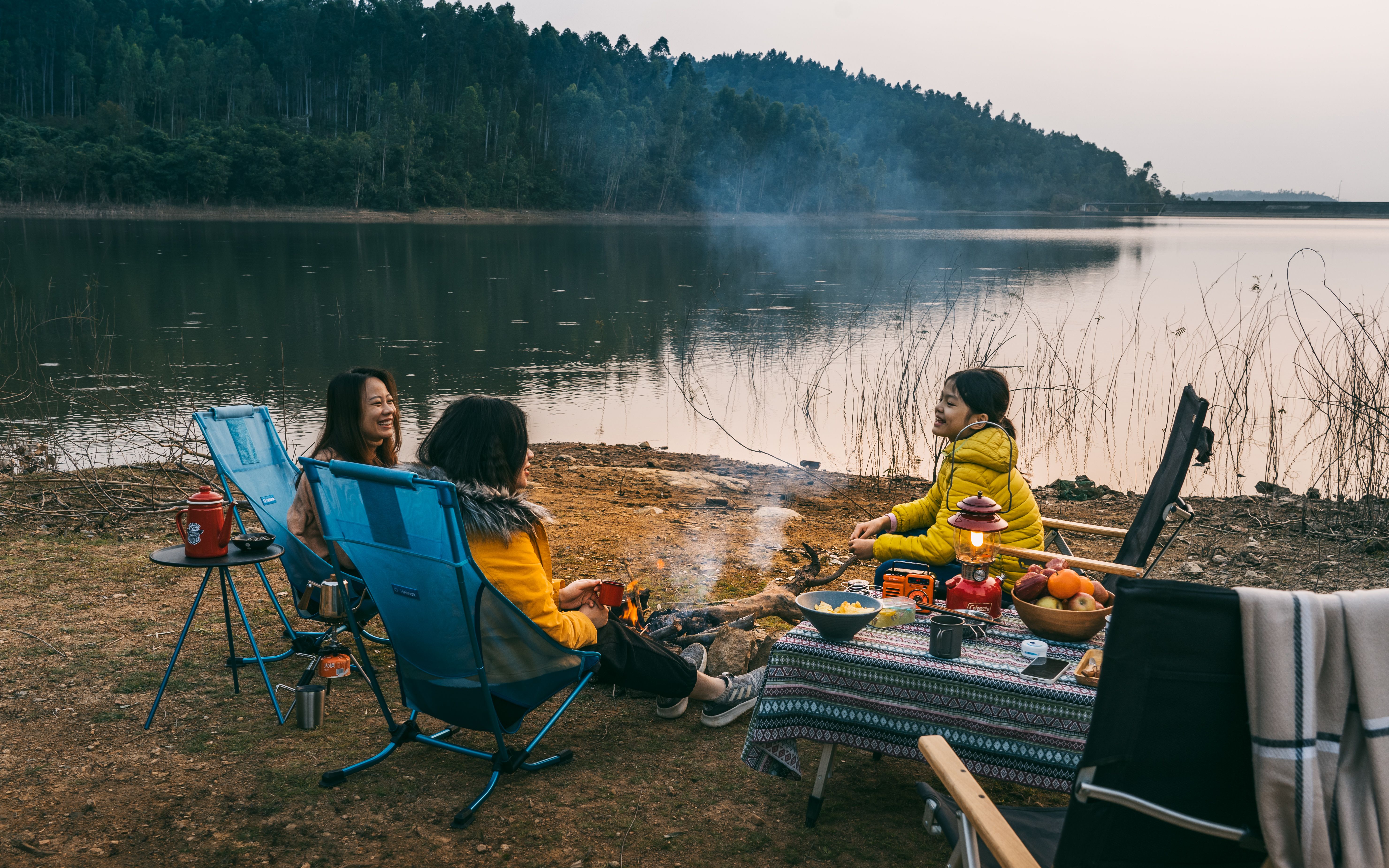 Cozy camping scene by a serene lake at sunset with friends enjoying a peaceful moment.