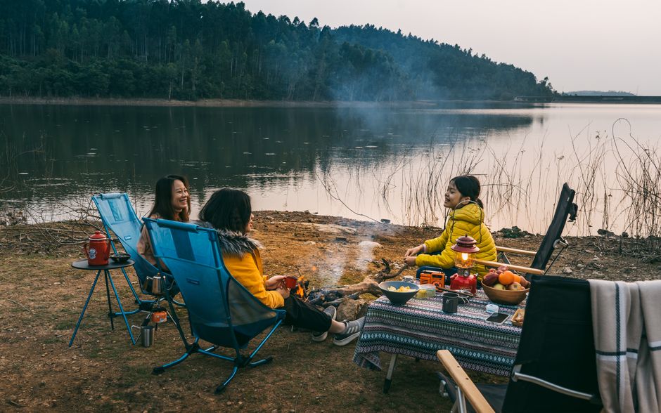 Cozy camping scene by a serene lake at sunset with friends enjoying a peaceful moment.