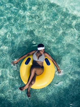 A woman in a striped bikini relaxes on a yellow float in a clear pool, enjoying a sunny day.
