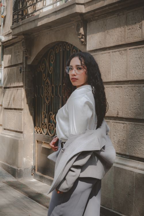 Free Woman in elegant attire walking in urban setting wearing glasses, exuding confidence. Stock Photo
