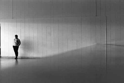 Free A woman stands alone in a minimalist room, casting shadows in black and white. Stock Photo