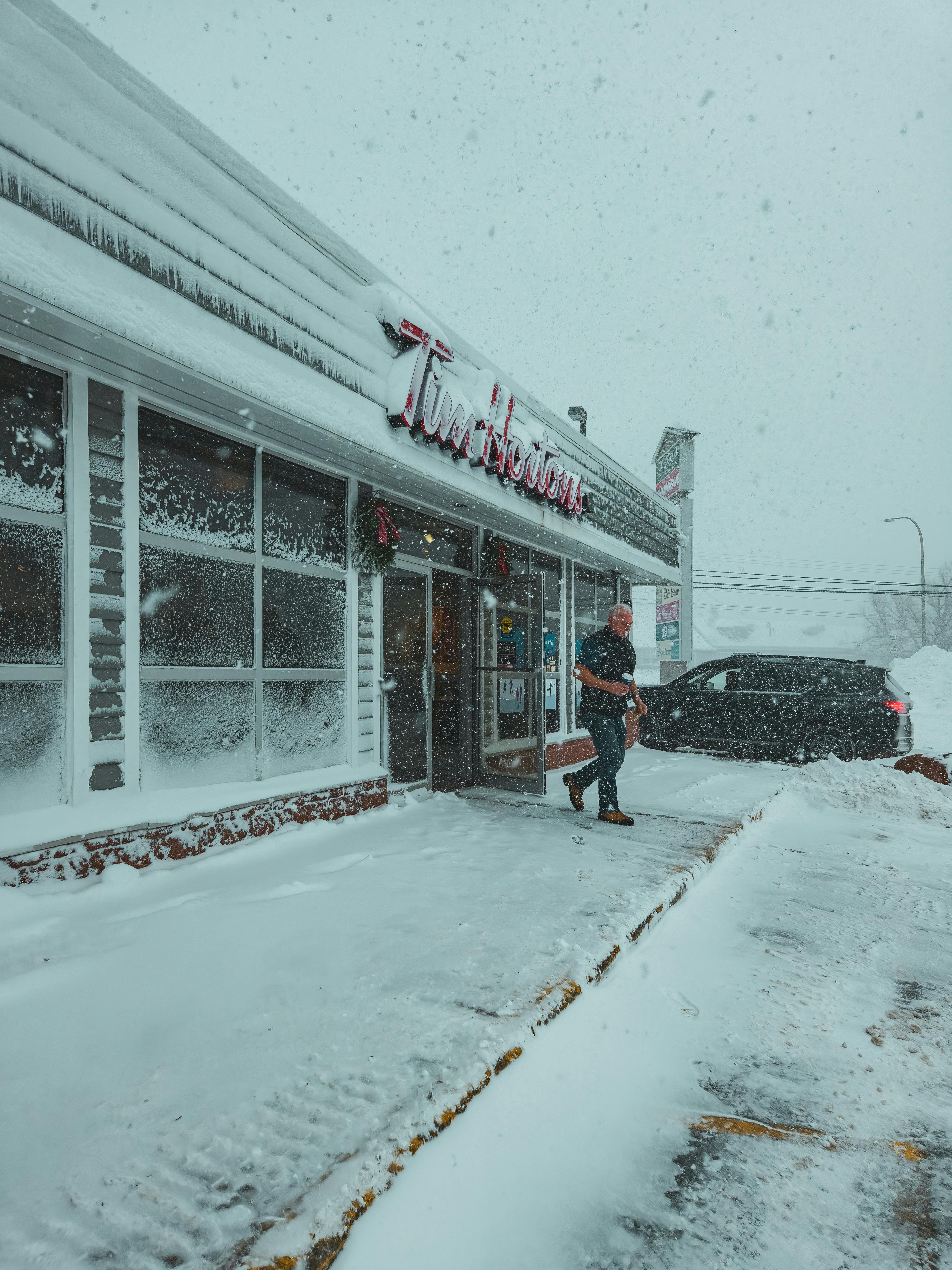 A snowy day outside a Tim Hortons with a person walking to a car.