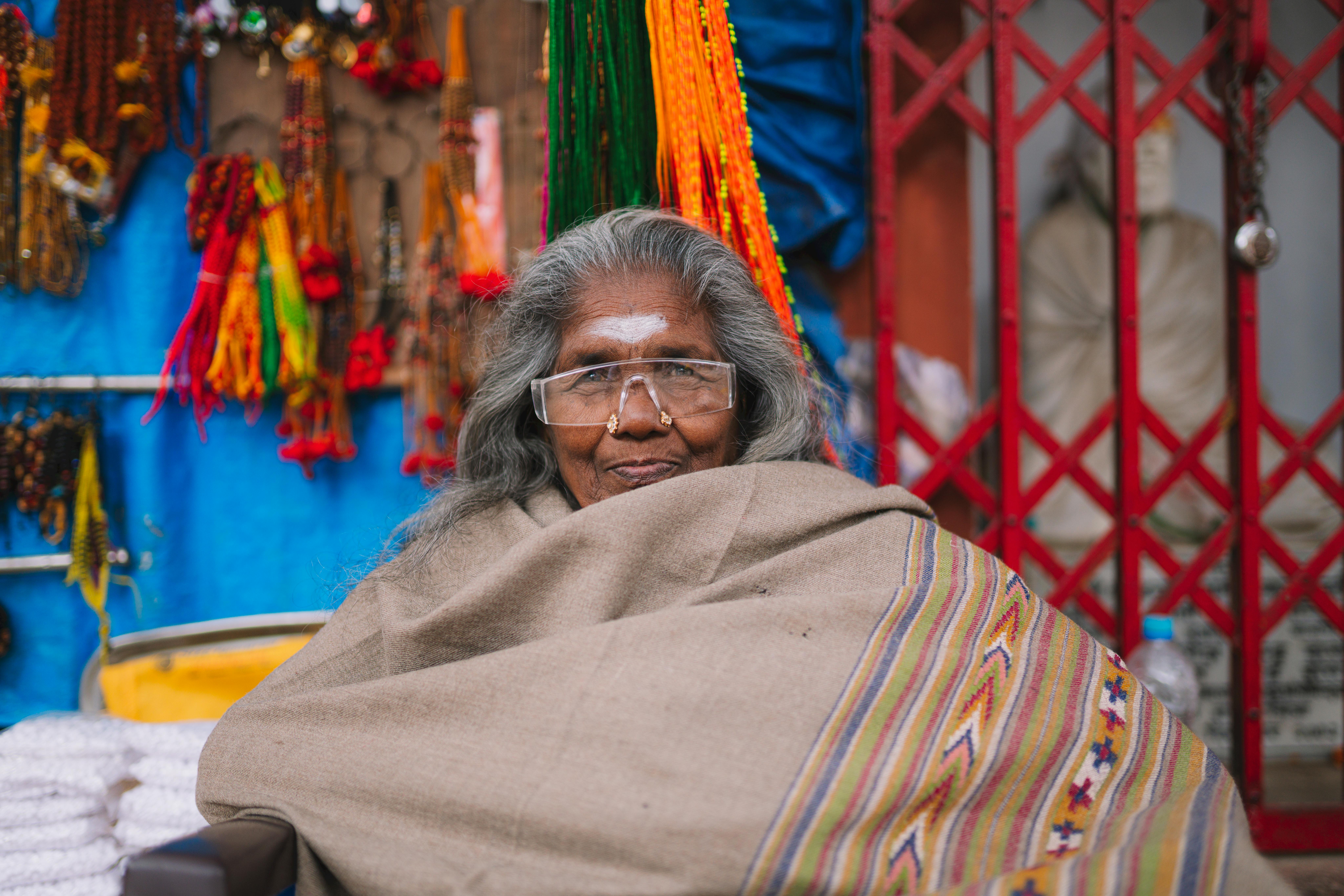 Candid portrait of a smiling elderly woman wrapped in a shawl, Varanasi market.